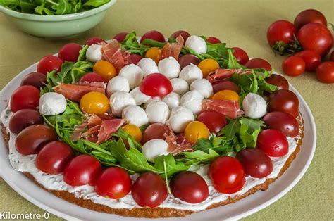 Une tarte salée colorée avec des tomates cerises, de la mozzarella, du basilic et de la charcuterie.