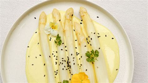 Asperges blanches servies avec une sauce crémeuse et de la poutargue râpée