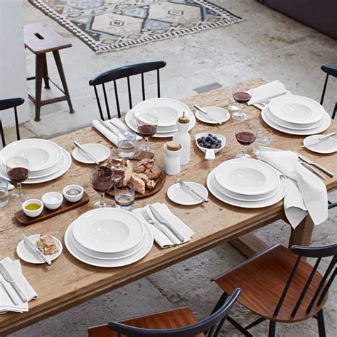 Photographie d'une table de cuisine joliment dressée avec une assiette Artesano Original Villeroy & Boch, sur laquelle repose une part de pizza appétissante, avec des éléments en bois et de l'ardoise.