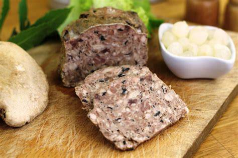 Terrine rustique de pâté de campagne aux trompettes de la mort, tranchée sur planche avec pain et pickles