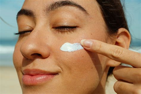 Une jeune femme appliquant délicatement une crème solaire sur son visage au soleil