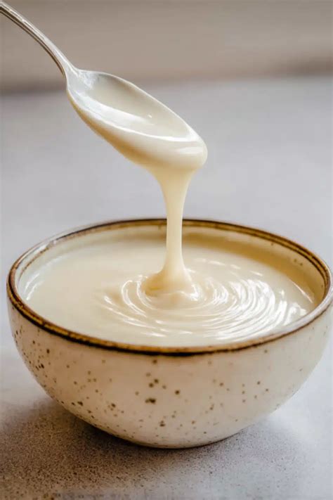 Une image montrant une sauce béchamel crémeuse dans un bol, avec des herbes fraîches parsemées sur le dessus.