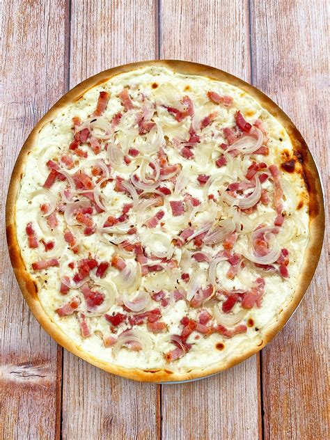 Tarte flambée garnie d'oignons et de lardons sur une planche en bois