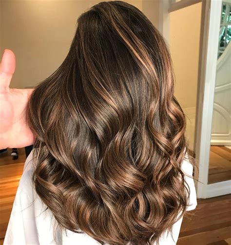 Modèle aux cheveux châtain foncé avec des reflets caramel foncé subtils.