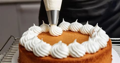 Une main utilisant une poche à douille pour former des meringues sur une plaque de cuisson