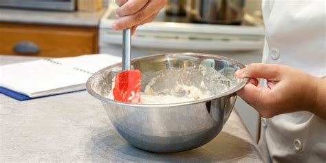 Main utilisant une maryse pour racler le fond d'un bol