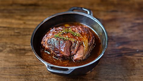 Un morceau de paleron de boeuf dans une cocotte avec des légumes et des herbes