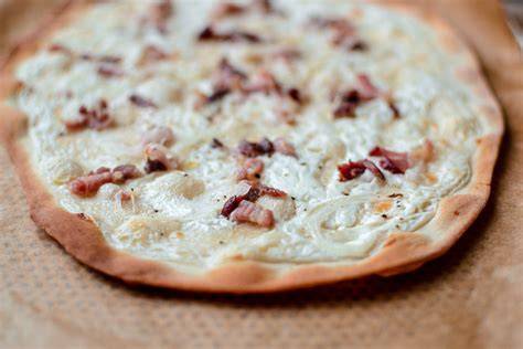 Schéma montrant les couches typiques d'une tarte flambée: pâte fine, crème épaisse, oignons, lardons